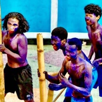 Four purple-painted men holding bamboo poles